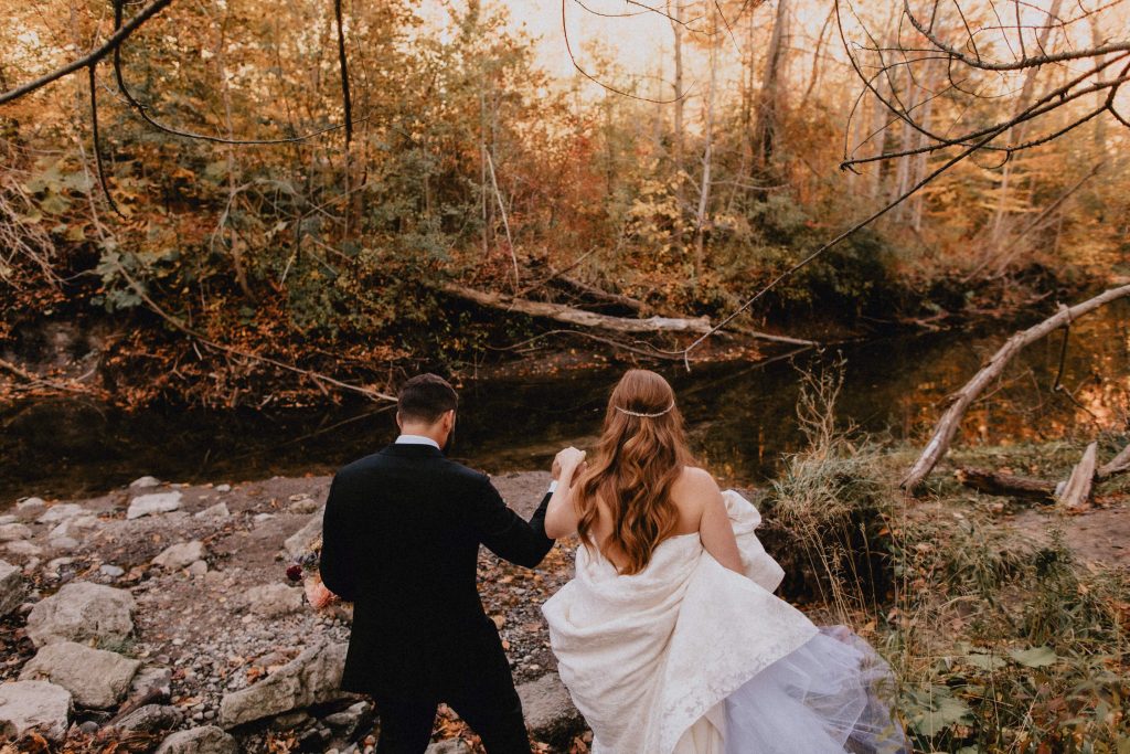Bride and groom walk through forest towards river - Autumn Micro Wedding at Berkeley Fieldhouse