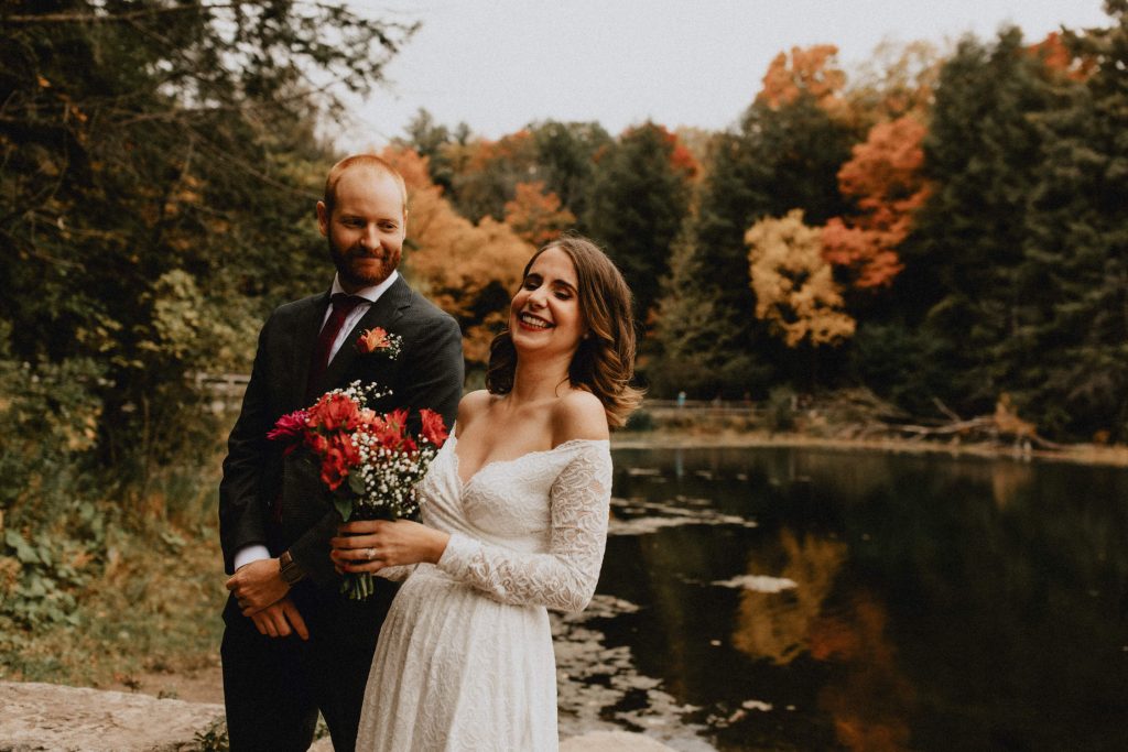 Bride laughs during fall wedding ceremony near pond - Huron Natural Area Micro Wedding Kitchener, Ontario